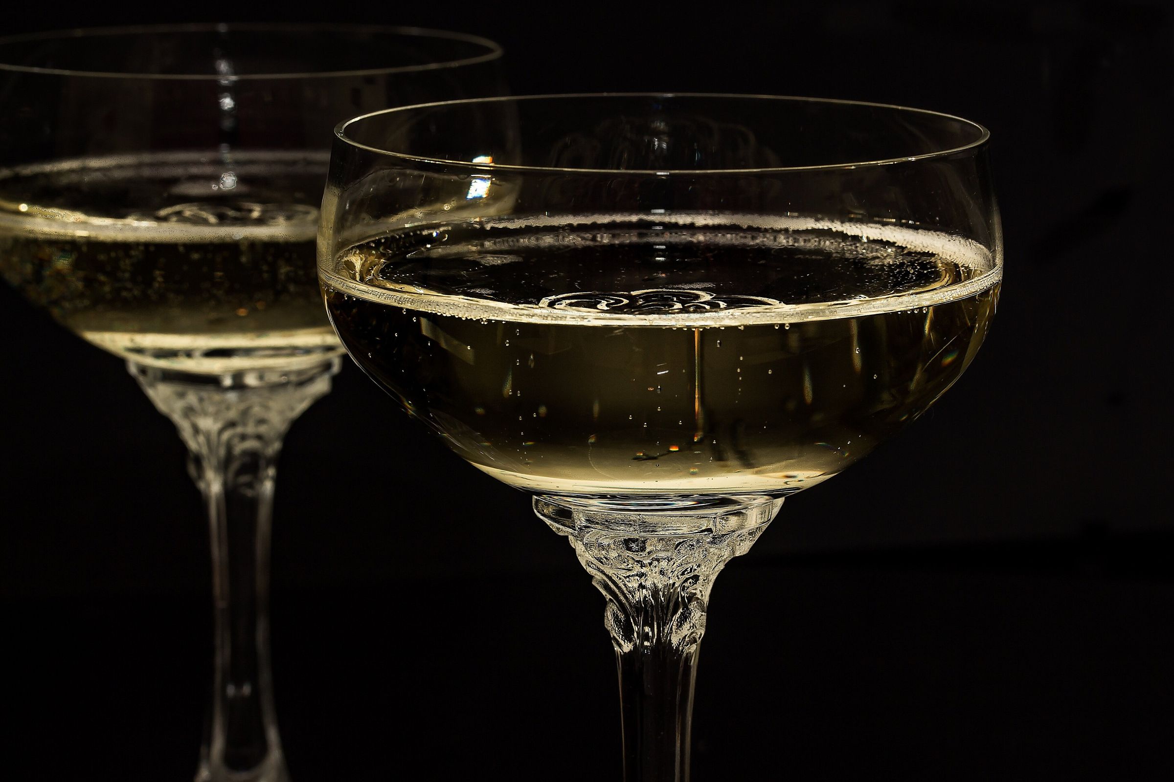 Two crystal coupes of sparkling champagne with ornate stems against a black background